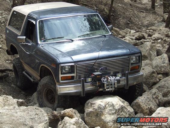 Dark SUV navigating a rocky trail, front 3/4 view. Appears to be from the early 1980s