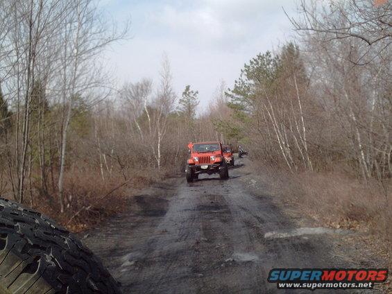 Red SUV driving away on a dirt road through trees