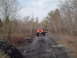 1991 Ford Bronco - A red SUV is seen from behind driving on a dirt road surrounded by trees in autumn.