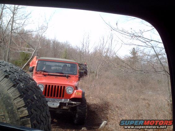 Orange Jeep Wrangler driving on a dirt trail with another Jeep behind it