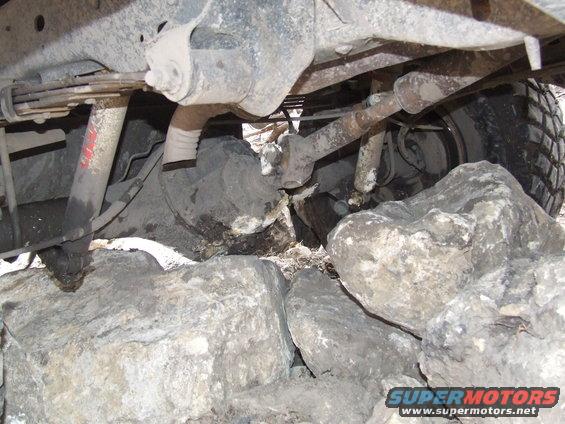 Undercarriage of a vehicle, showing suspension and tire, resting on large rocks