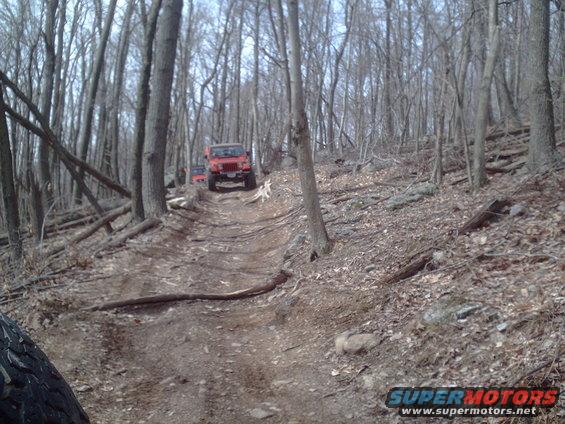 Red Jeep Wrangler driving up a dirt path in a forest