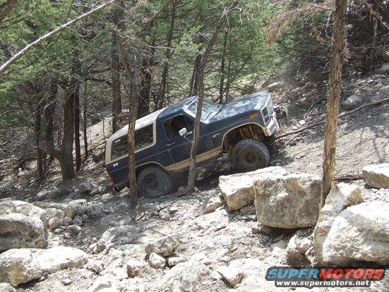 1986 Ford Bronco climbing over rocks on a wooded trail