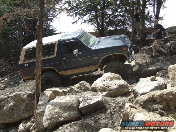 Dark blue Ford Bronco with tan top climbing over large rocks on a trail