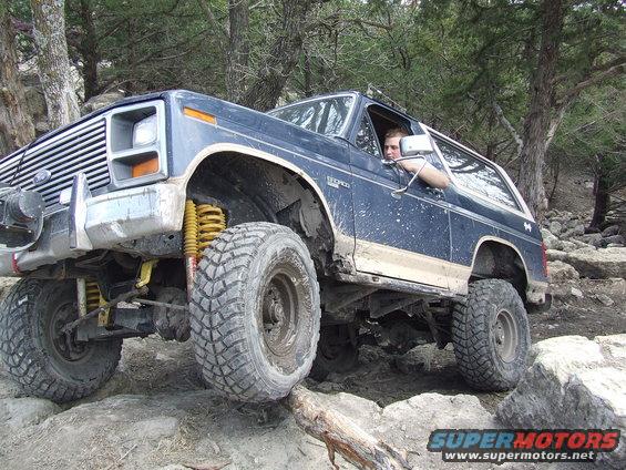 Dark blue Ford Bronco with lifted suspension and large tires navigating a rocky trail