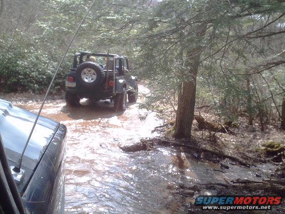 Black Jeep Wrangler driving through mud on a wooded trail