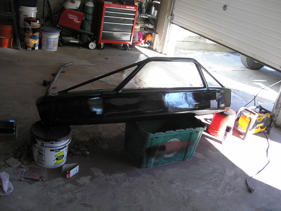 Black car body with a roll cage, resting on buckets in a garage