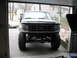 1994 Ford Bronco - This lifted Ford truck is parked inside a garage, showing its front end and suspension modifications.