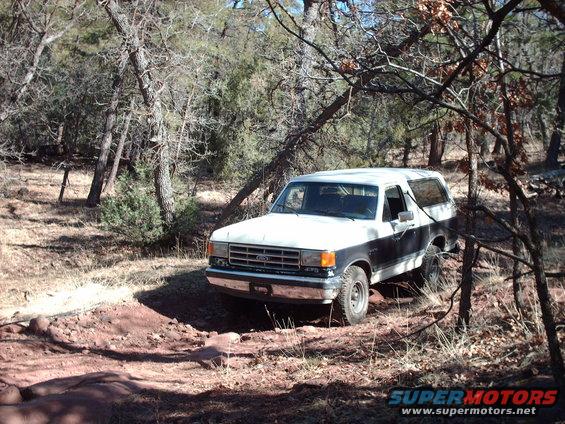 1988 Ford Bronco driving on a dirt trail through trees