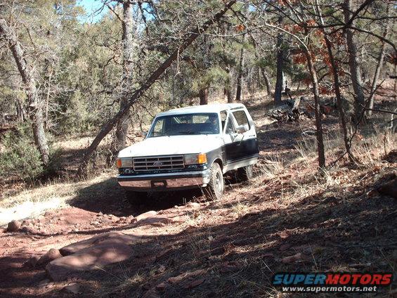 Two-tone white and dark blue Ford Bronco on a dirt trail, front-left view