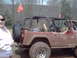 1991 Ford Bronco - A red Jeep Wrangler, covered in mud, is parked outdoors with two orange flags visible.