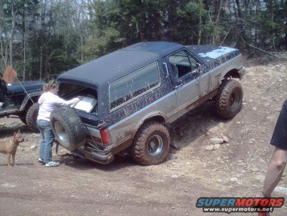 1991 Ford Bronco on a dirt trail with a woman loading items into the rear and another Jeep visible