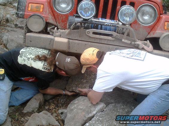 Red Jeep Wrangler stuck on rocks, two people trying to free it