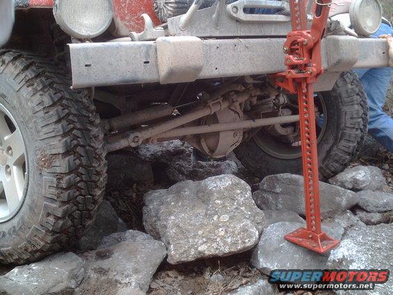 Off-road vehicle's rear axle and tires on rocks with a Hi-Lift jack