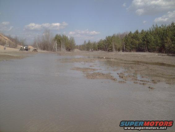 Two off-road vehicles are visible in a muddy, watery landscape with trees in the background