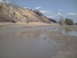 1991 Ford Bronco - A wide view of a muddy, wet landscape with a sand dune and scattered trees under a partly cloudy sky.