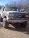 1991 Ford Bronco - This lifted Ford Bronco is covered in mud, suggesting it has been off-roading. Another vehicle is partially visible to the right.