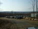 1991 Ford Bronco - A large group of SUVs and trucks are parked in a lot surrounded by trees and hills.