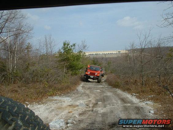 Orange Jeep Wrangler driving off-road with another vehicle behind it
