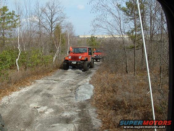 Orange Jeep Wrangler on a rocky dirt road, with another Jeep behind it
