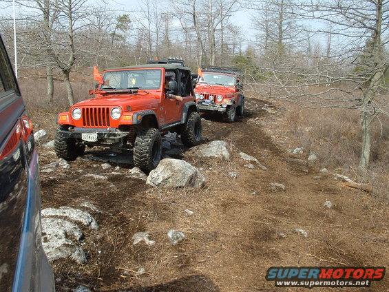 Two orange Jeep Wranglers on a rocky trail, one in foreground, another behind it