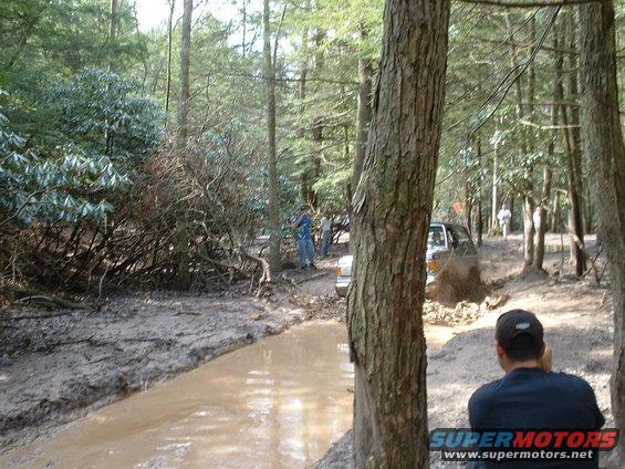 Silver Ford Bronco driving through mud in a forest