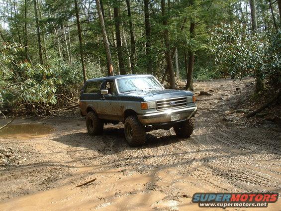 1991 Ford Bronco driving through a muddy forest trail