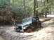 1991 Ford Bronco - A Jeep Wrangler navigates a challenging muddy off-road course surrounded by trees.