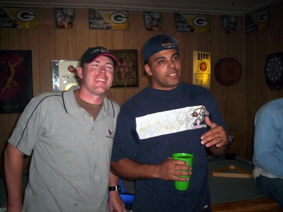 Two men in a room with wood paneling, Green Bay Packers banners, and a dartboard