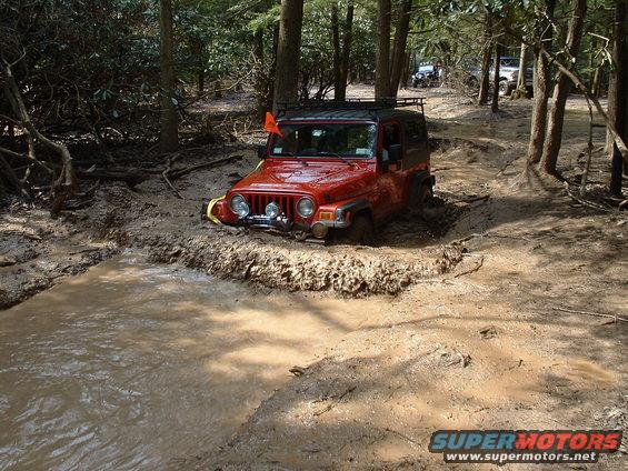 Red Jeep Wrangler stuck in mud, with other vehicles in background