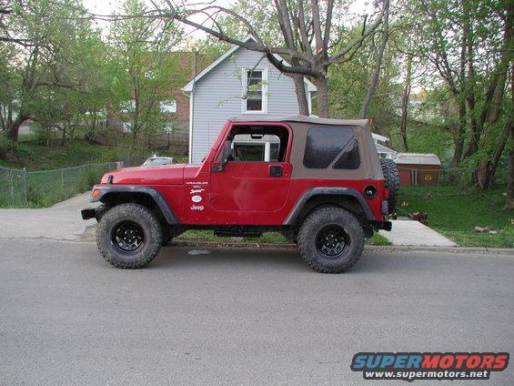 Red Jeep Wrangler with a tan soft top, black wheels, and off-road tires, viewed from the side