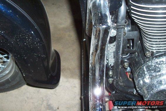 Close-up of motorcycle engine fins, chrome pipes, and part of a black fender