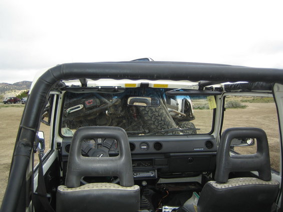 Interior of a white Suzuki Samurai with roll cage and spare tire visible through windshield