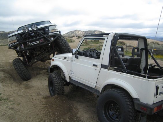 White Suzuki Samurai next to a lifted white Ford Bronco off-roading
