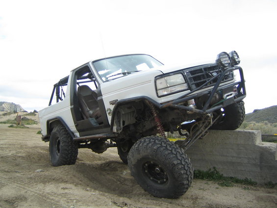 White off-road vehicle with roll cage and large tires, front right tire on concrete step