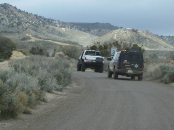 Black SUV with 'SHERIFF' text and a white pickup truck on a dirt road