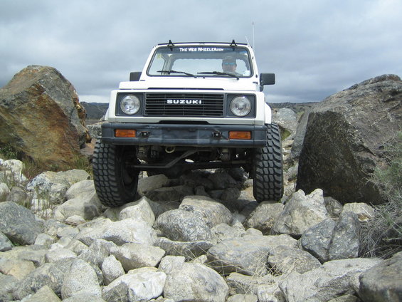 White 1987 Suzuki Samurai on rocks, front view. The Web Wheeler.com sticker on windshield