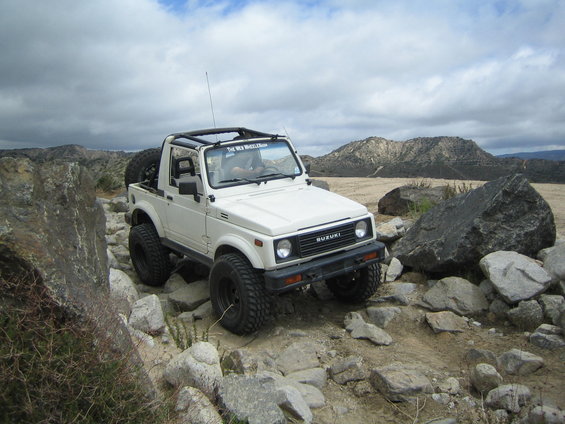 White 1987 Suzuki Samurai navigating a rocky trail with mountains in the background