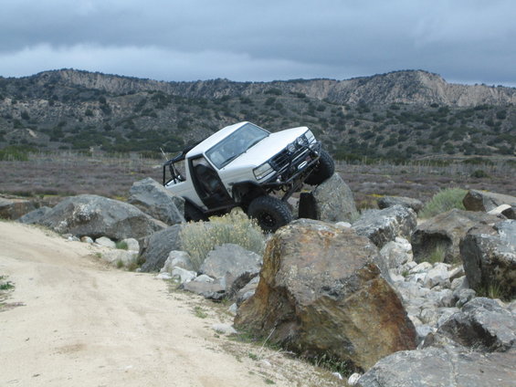 White 1987 Suzuki Samurai with off-road modifications navigating large rocks