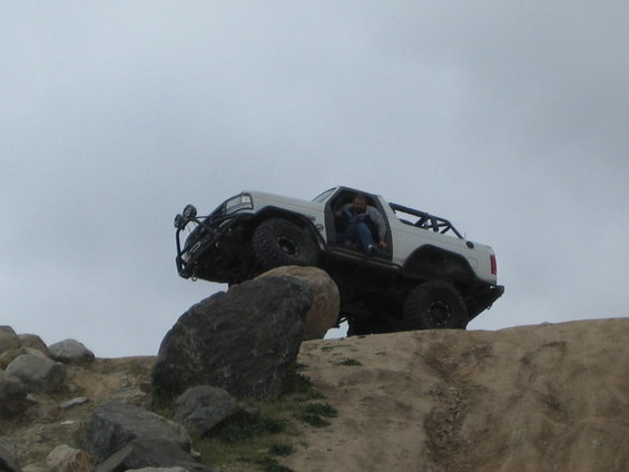 White off-road vehicle with roll cage climbing over rocks
