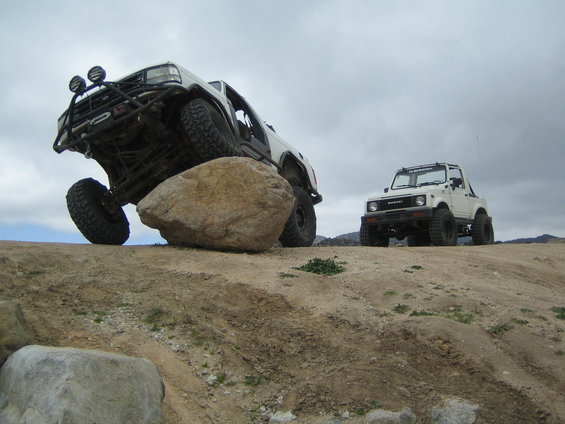 1987 Suzuki Samurai and a larger off-road vehicle on a dirt hill with rocks