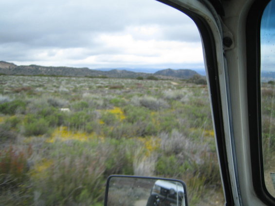 view from inside a vehicle looking out at a dry, scrubby landscape with hills in the distance