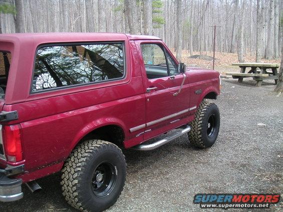 Red Ford Bronco with off-road tires and side steps parked on gravel