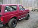 1994 Ford Bronco - A red Ford Bronco with off-road tires sits parked in a wooded area next to a picnic table.