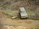 1989 GMC Jimmy - This GMC SUV is navigating a muddy creek on an off-road trail, with trees and debris on the surrounding slopes.