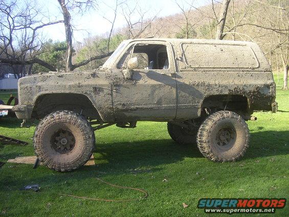 Mud-covered SUV with large tires, lifted suspension, and a removable hardtop, viewed from the side
