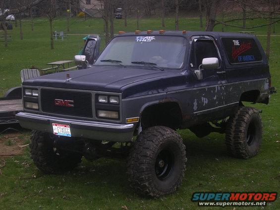 Dark blue 1989 GMC Jimmy lifted with off-road tires, front 3/4 view