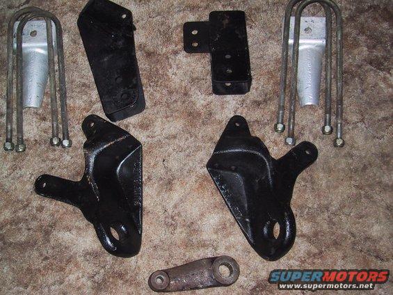 Several black and silver metal vehicle suspension parts, including U-bolts and brackets, laid out on a textured surface