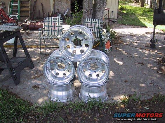Five aluminum wheels stacked on concrete, with chairs and a ladder in the background