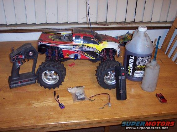 RC monster truck with remote, fuel, and parts on a wooden table